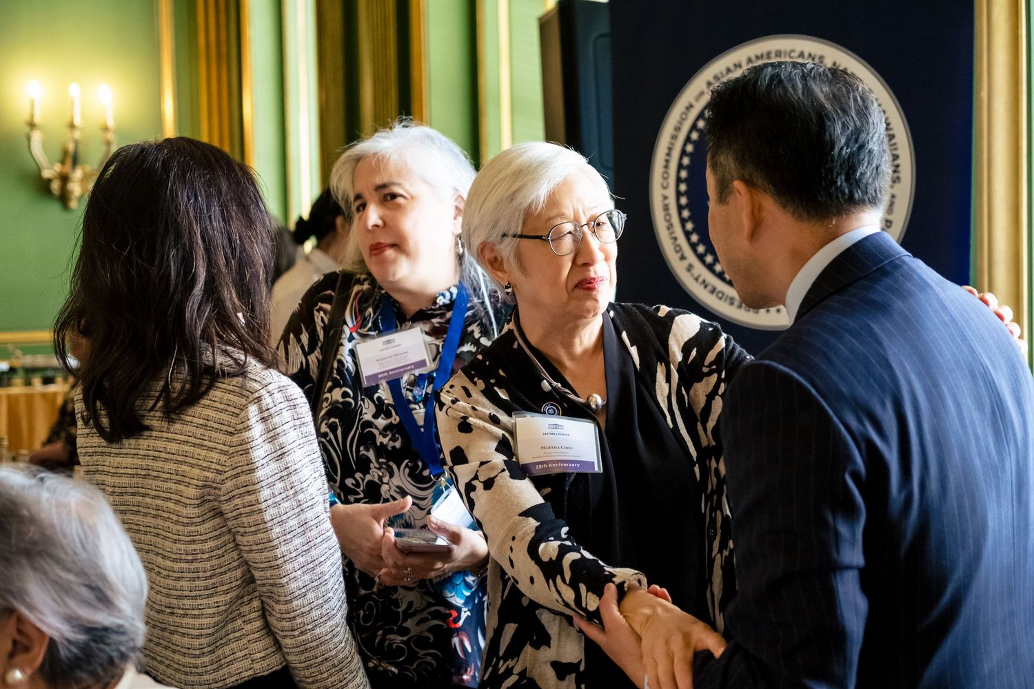 Professionals networking at a formal government event near a presidential seal in an elegant green room.
