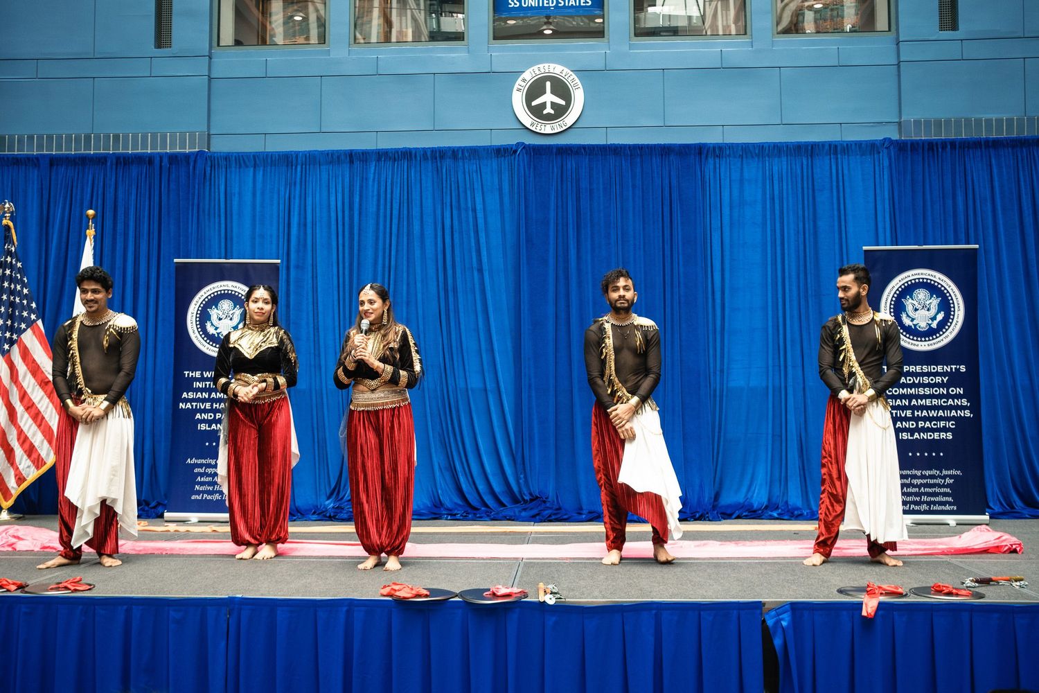 Indian classical dancers perform on stage at a formal government event with blue backdrop and American flag.