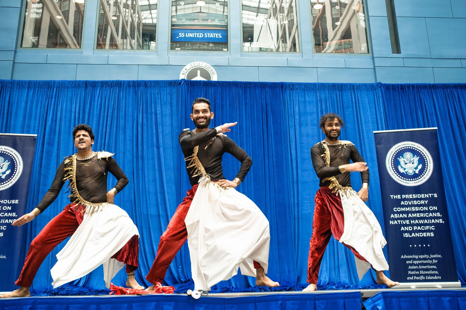 Three male dancers perform traditional Indian dance on stage at a U.S. government advisory conference event.