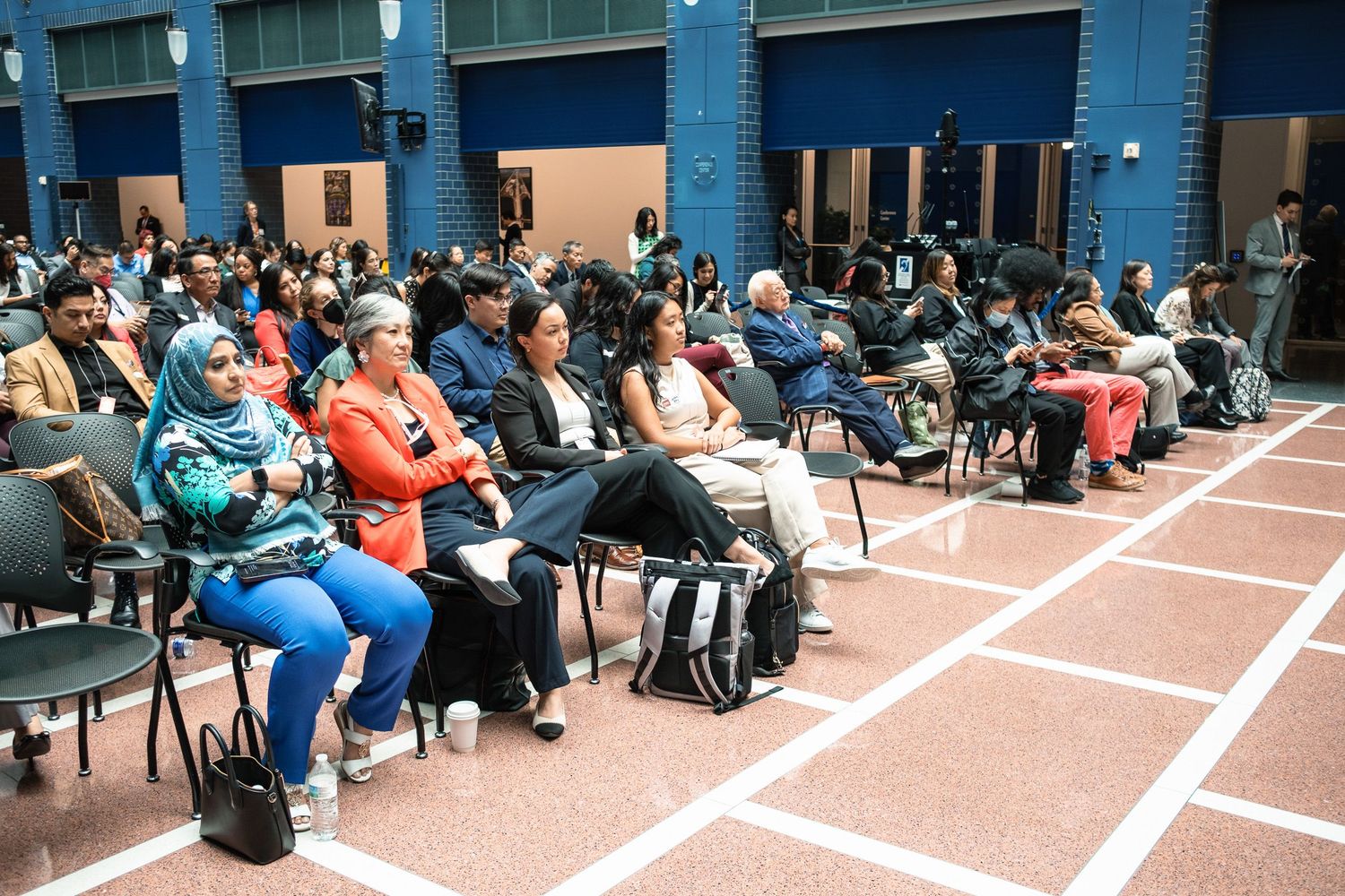 Diverse audience seated in rows at a formal government event, including woman in hijab and attendees in professional attire.