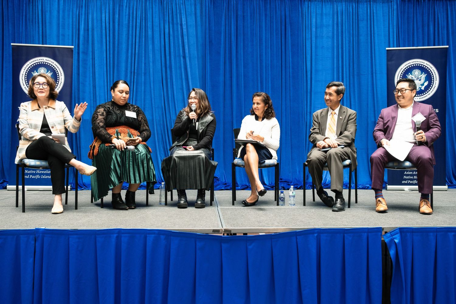 Six panelists seated on stage at professional conference in front of blue backdrop with organization logos.