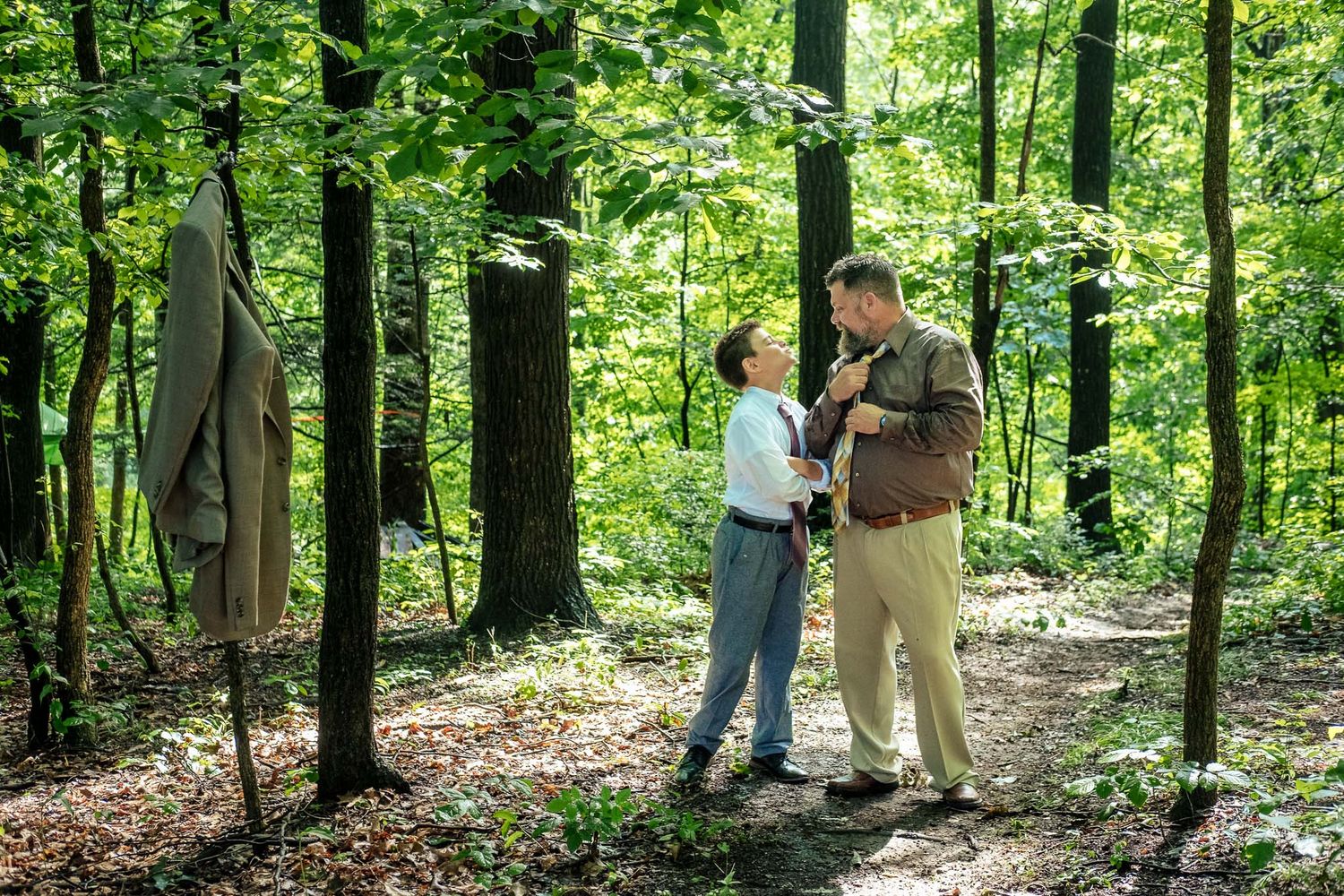 Couple sharing a romantic moment in a sunlit forest clearing surrounded by tall green trees.