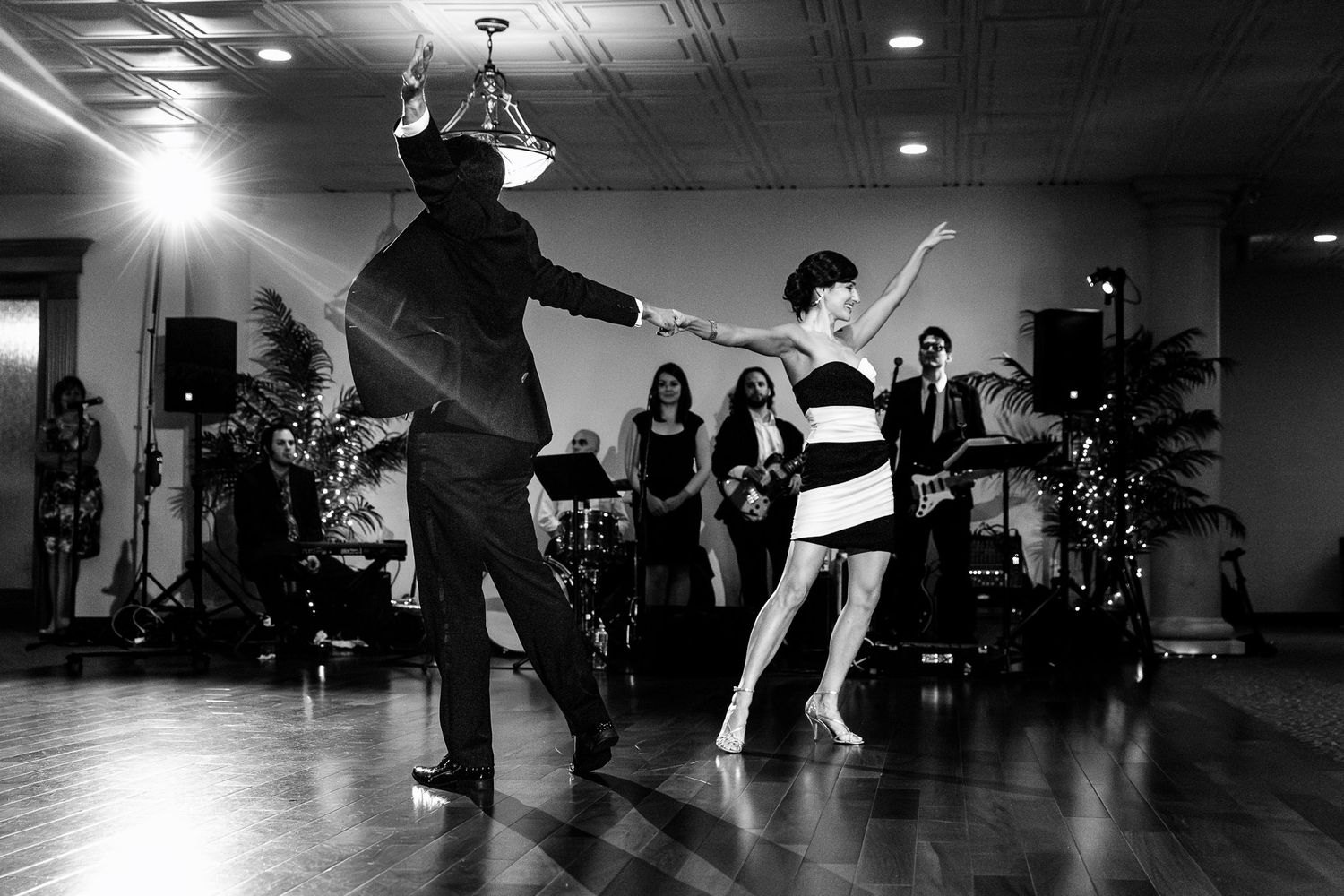 Couple performs energetic dance at wedding reception while guests watch in black and white photo.