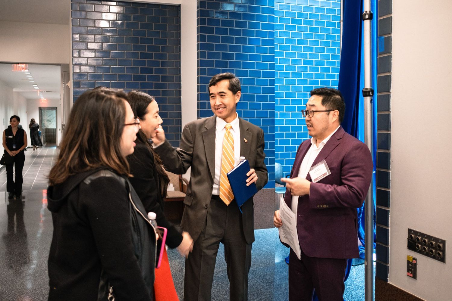 Professionals networking in a hallway with blue tile wall at a formal business event.
