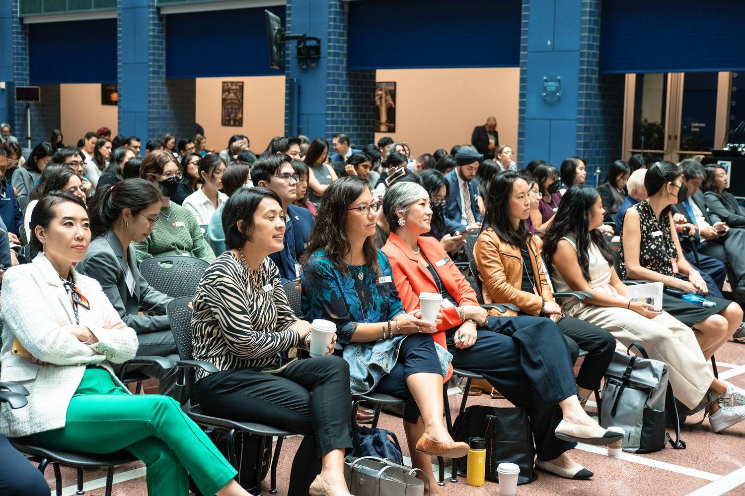 Diverse audience seated in rows at an indoor conference or cultural event, attentively listening to a presentation.