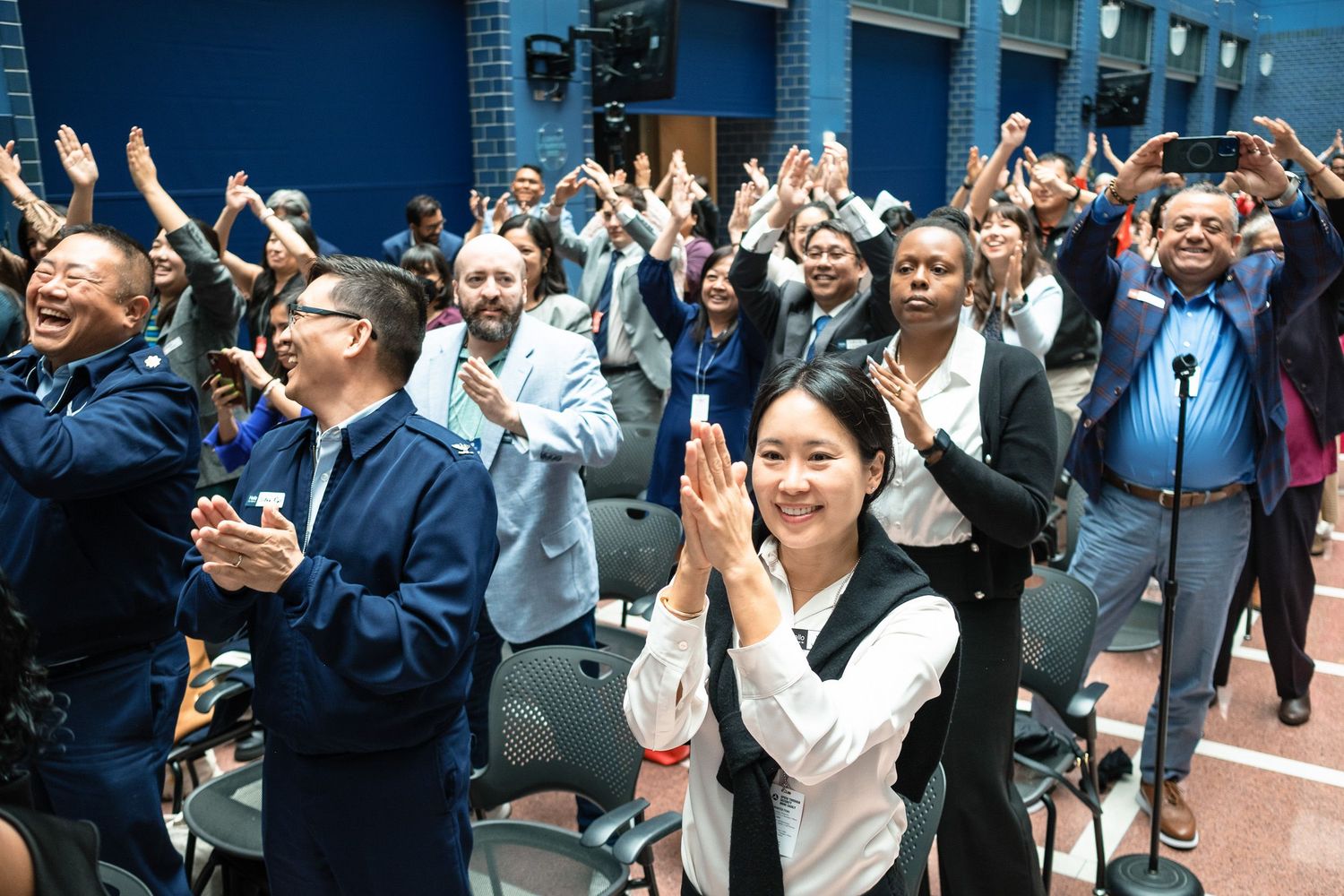 Diverse crowd of attendees applauds enthusiastically at an indoor community event or conference.