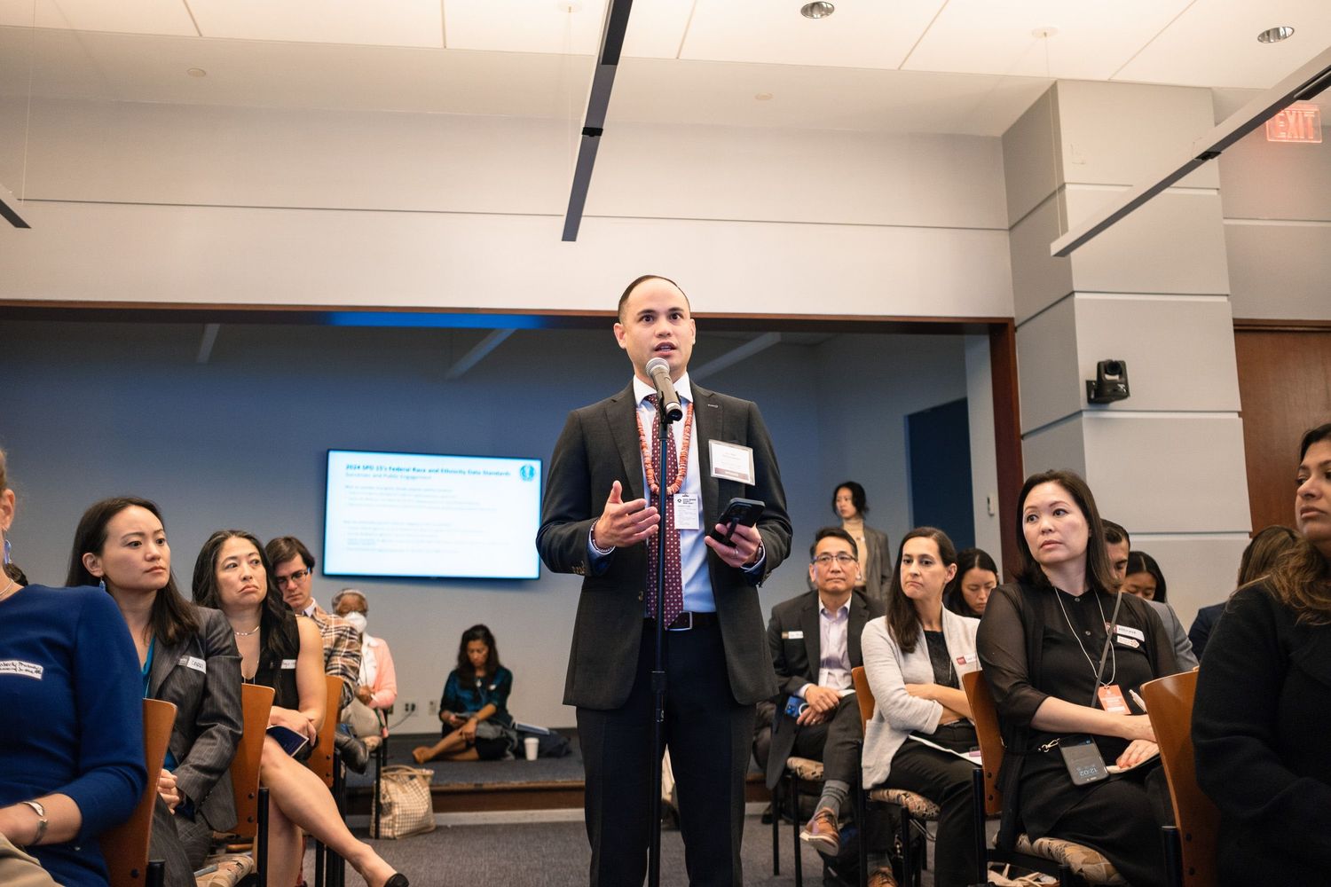 Professional speaker addresses diverse audience at corporate conference event in modern meeting room.