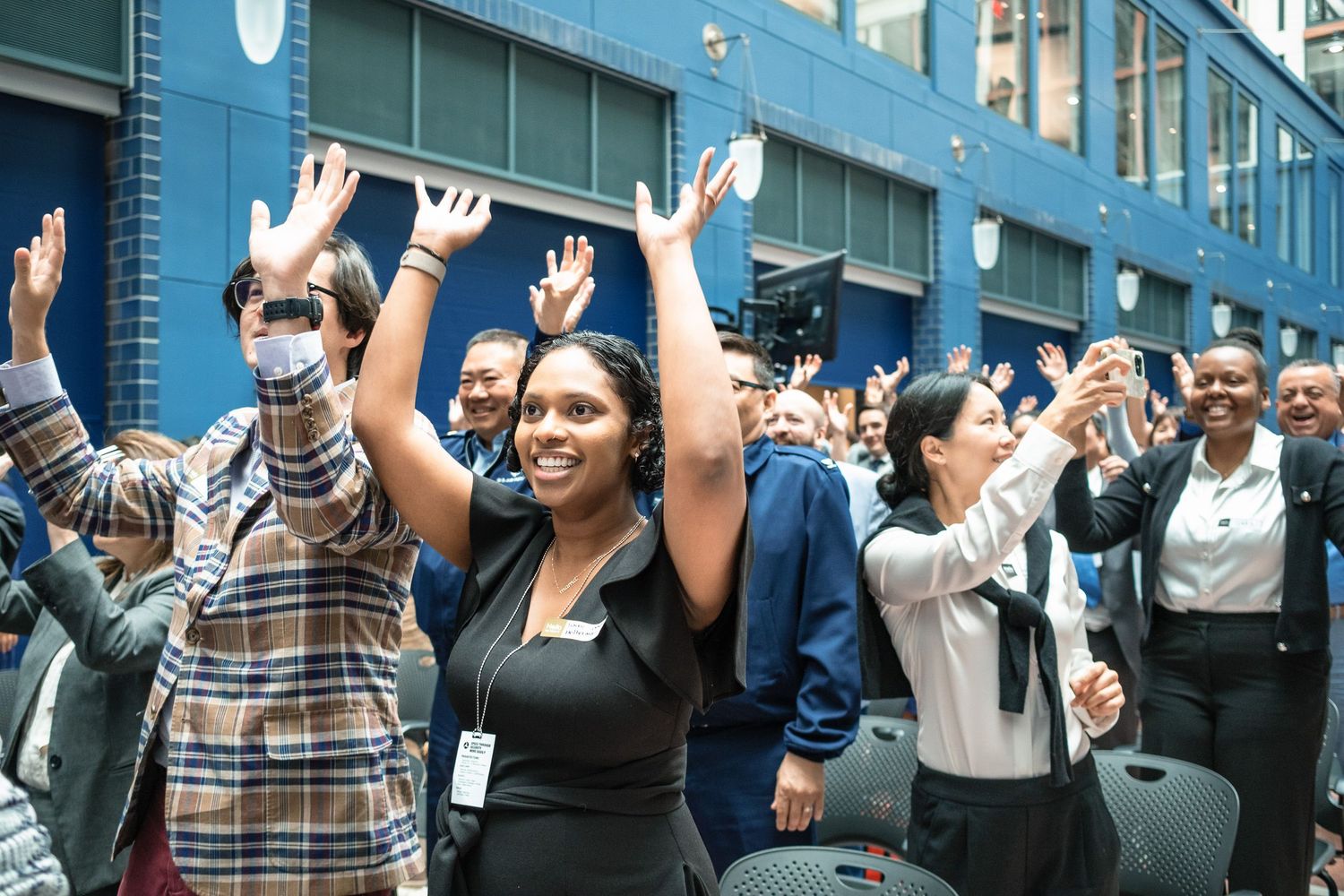 Diverse group of professionals clapping and celebrating at a corporate event outdoors near a blue building.