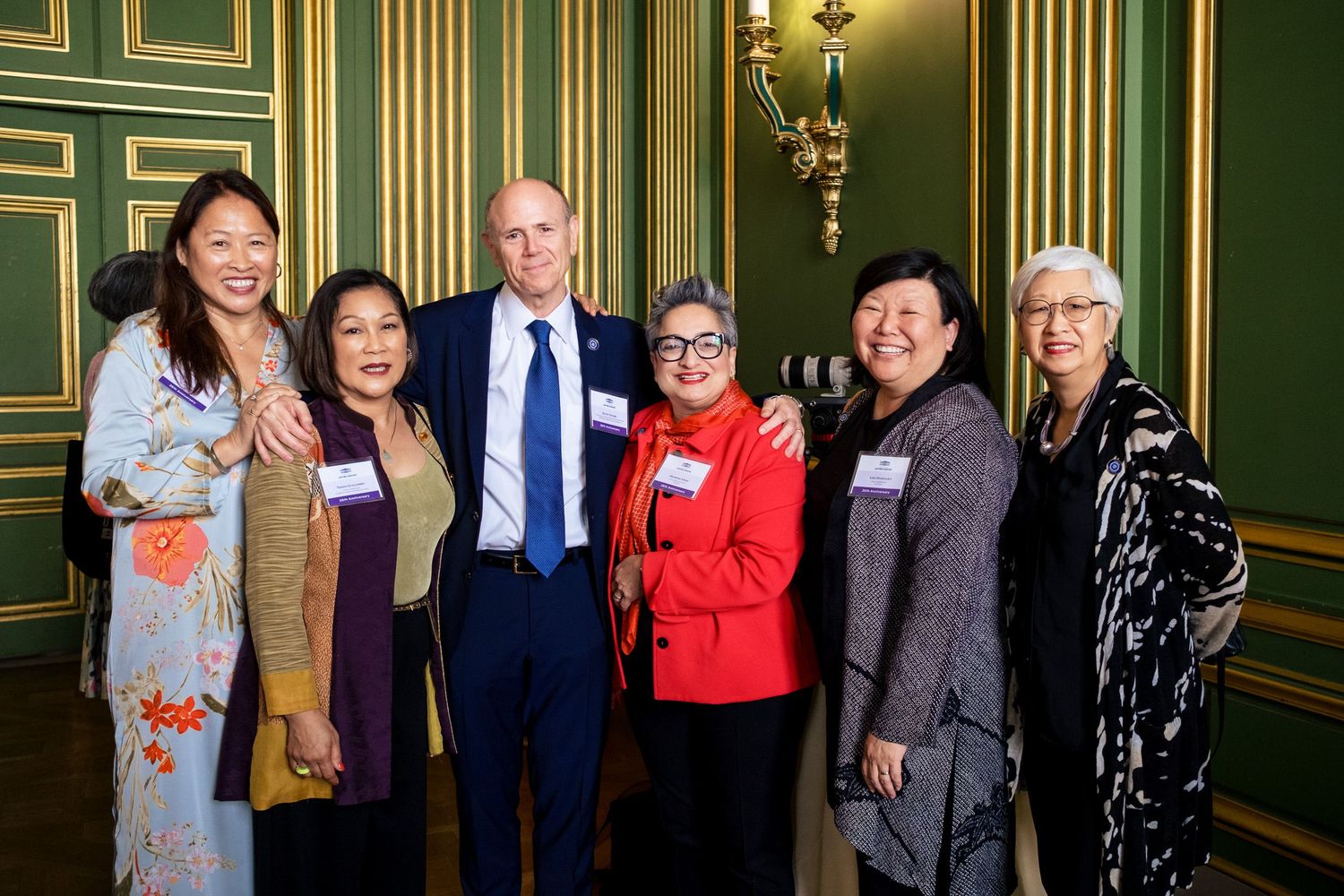 Group of six professionals smiling together in an elegant green-walled room at a formal networking event.