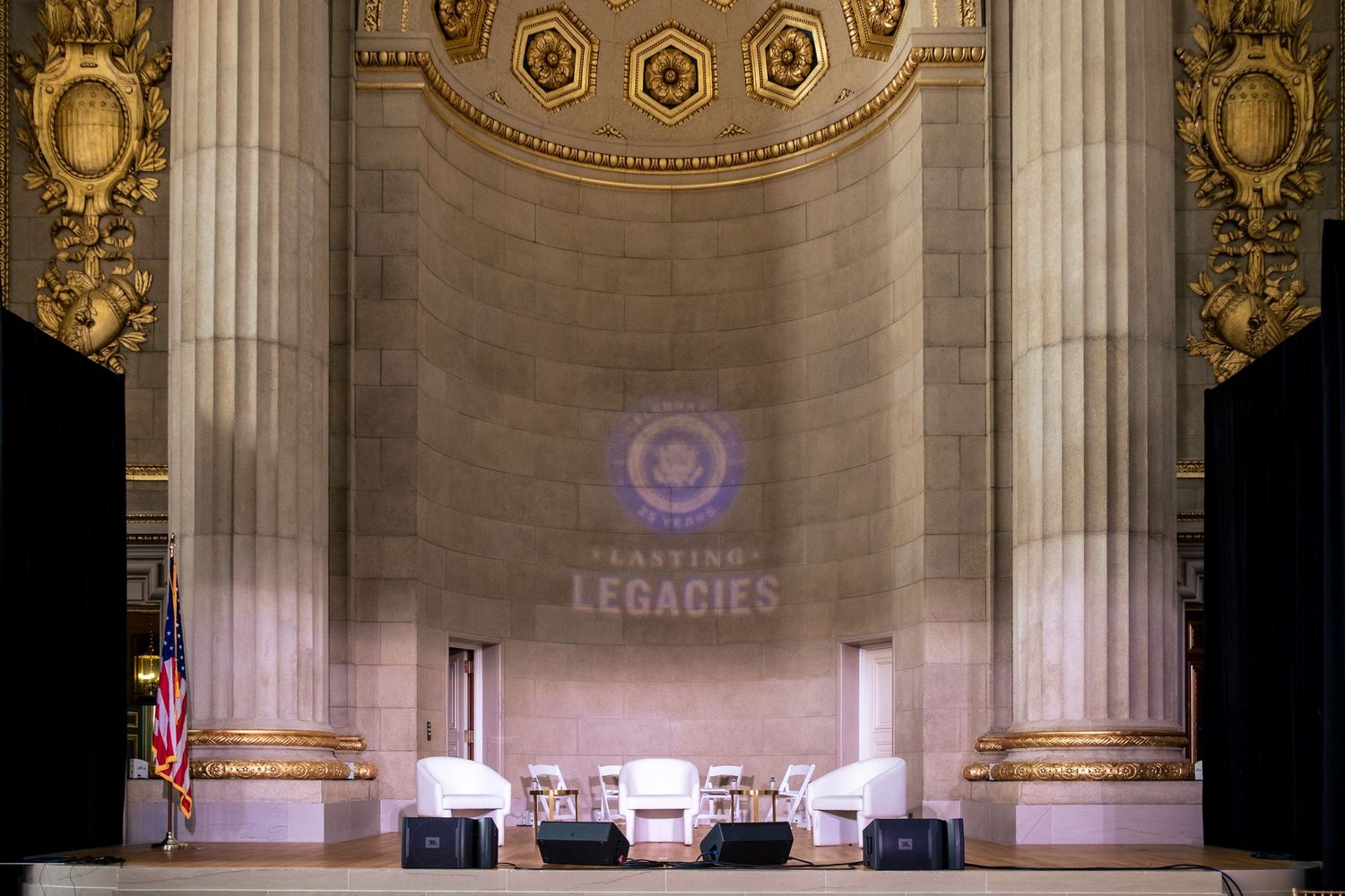 Grand hall stage with columns, white chairs, and a projected 