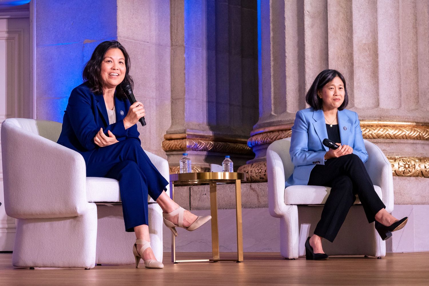 Two women in business attire seated on stage during a panel discussion at a formal event.