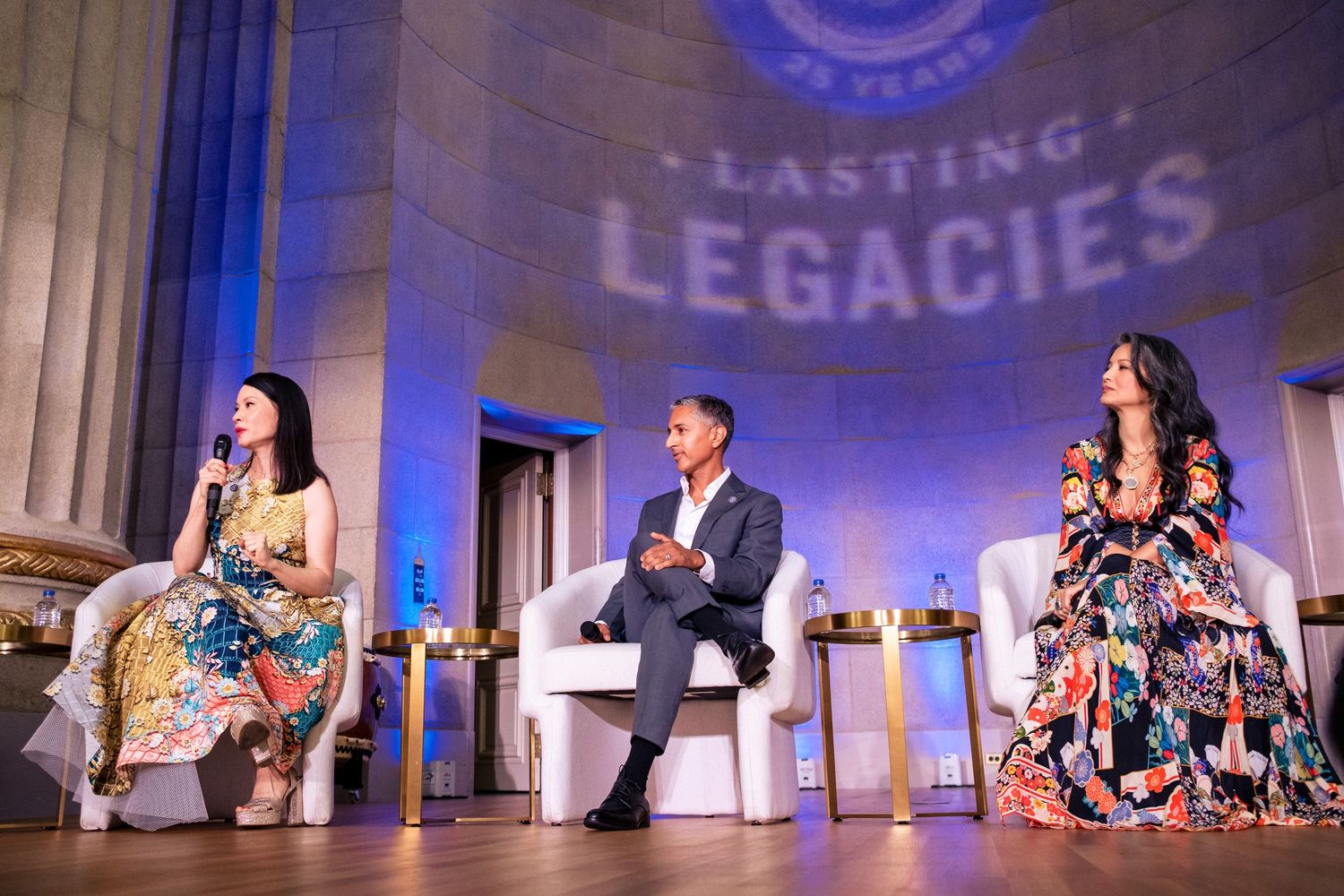 Three panelists sit on stage beneath Lasting Legacies projection at formal anniversary event.