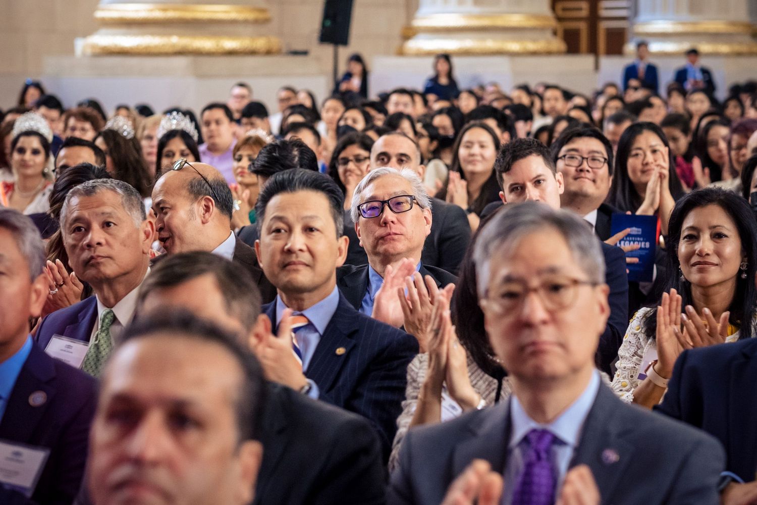 Diverse audience clapping at a formal event in an elegant hall, featuring attendees in business attire.