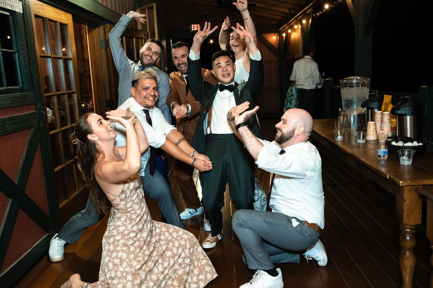 Wedding guests dance and celebrate energetically with a groom in a bow tie at the reception.