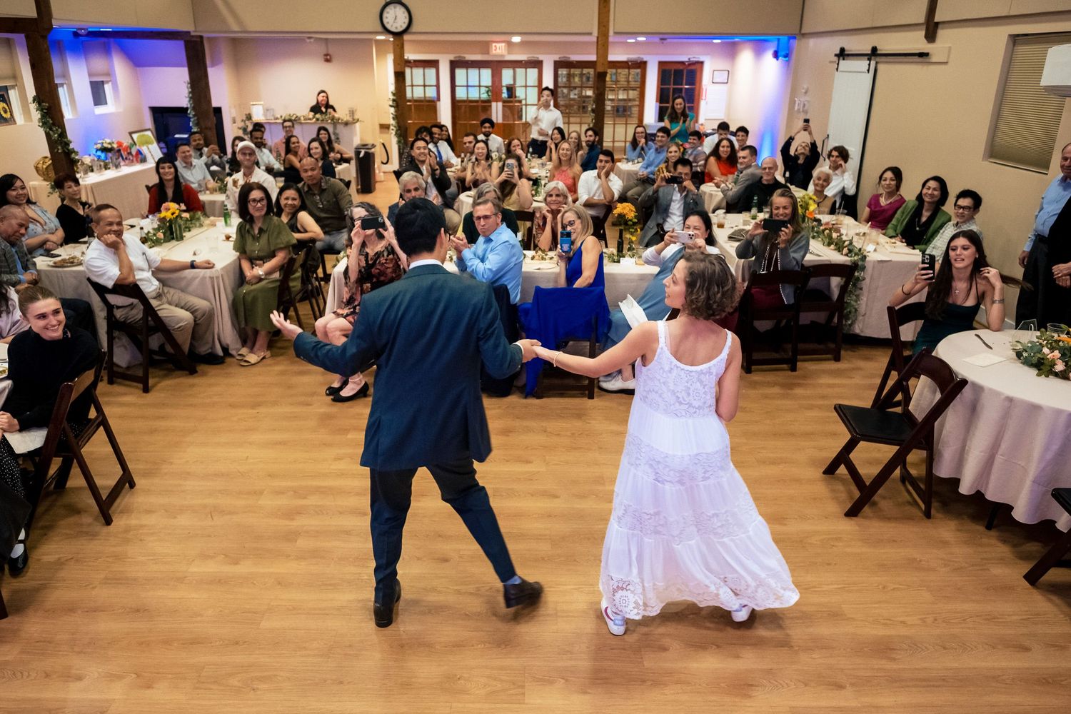 Bride and groom share their first dance on the wooden dance floor surrounded by wedding guests.