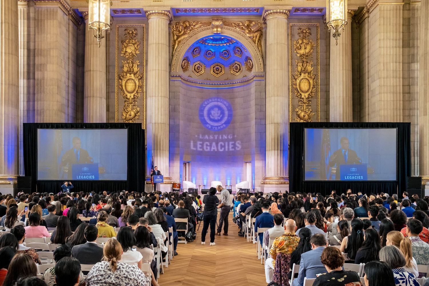 Large audience gathered at an elegant venue for the Creating Legacies conference, featuring grand architecture and large screens.