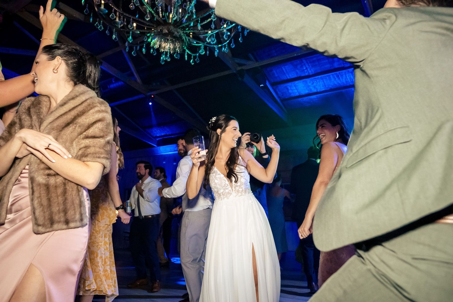 Bride dancing joyfully with guests on crowded wedding reception dance floor.