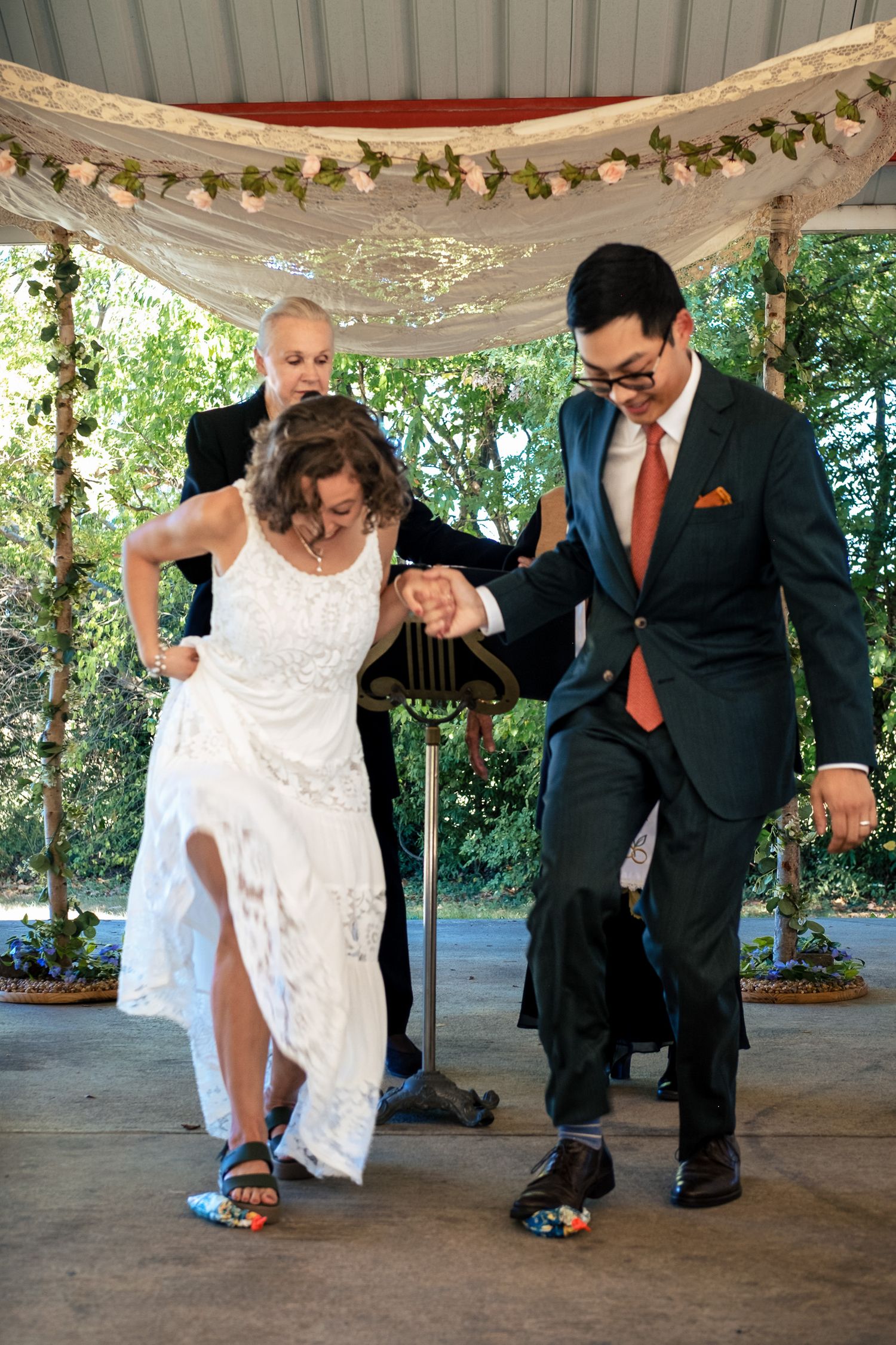 Bride and groom stomp on wrapped glasses in traditional Jewish wedding ceremony with officiant assisting.