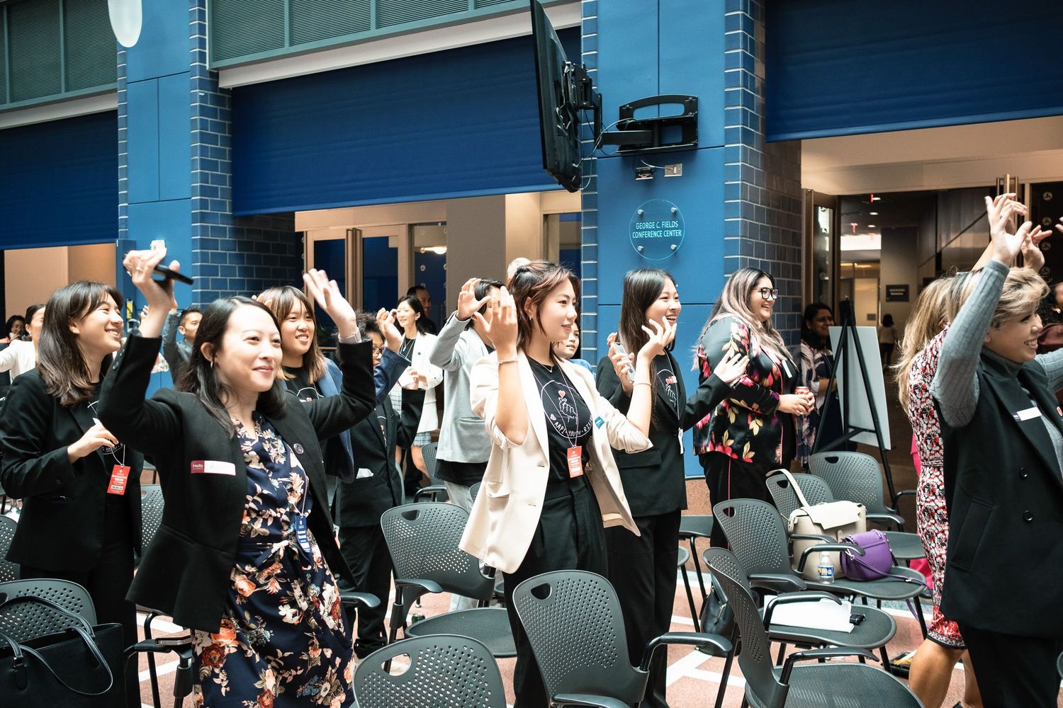 Diverse group of women celebrating and raising hands at a professional networking event indoors.