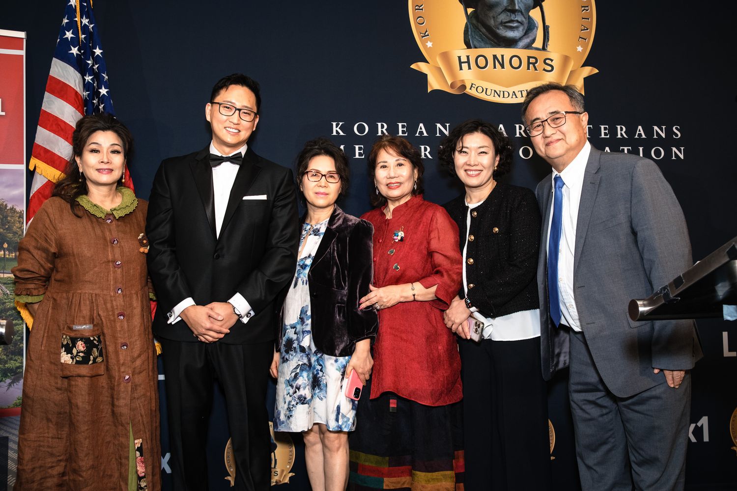 Six people posing together at Korean War Veterans Memorial Foundation Honors event with American flag backdrop.