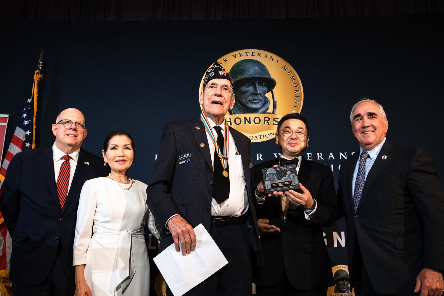 Veterans honored at ceremony with officials posing on stage before a gold medallion backdrop at an awards event.