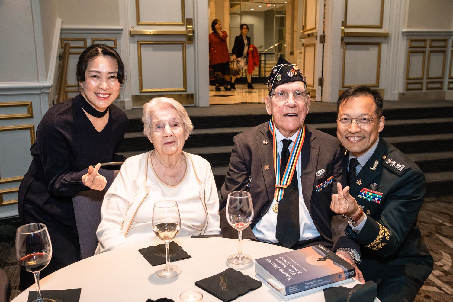 Four guests pose smiling at a formal gala dinner table with wine glasses.