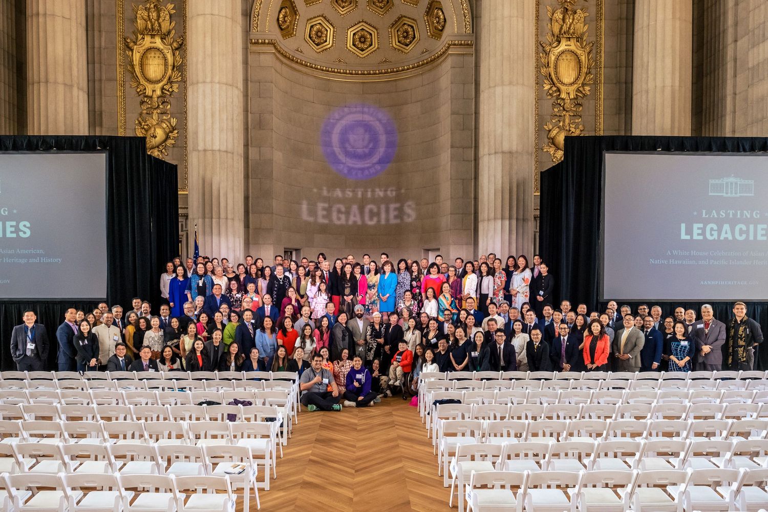 Large group photo at Daring Legacies conference in ornate hall with screens displaying event branding.