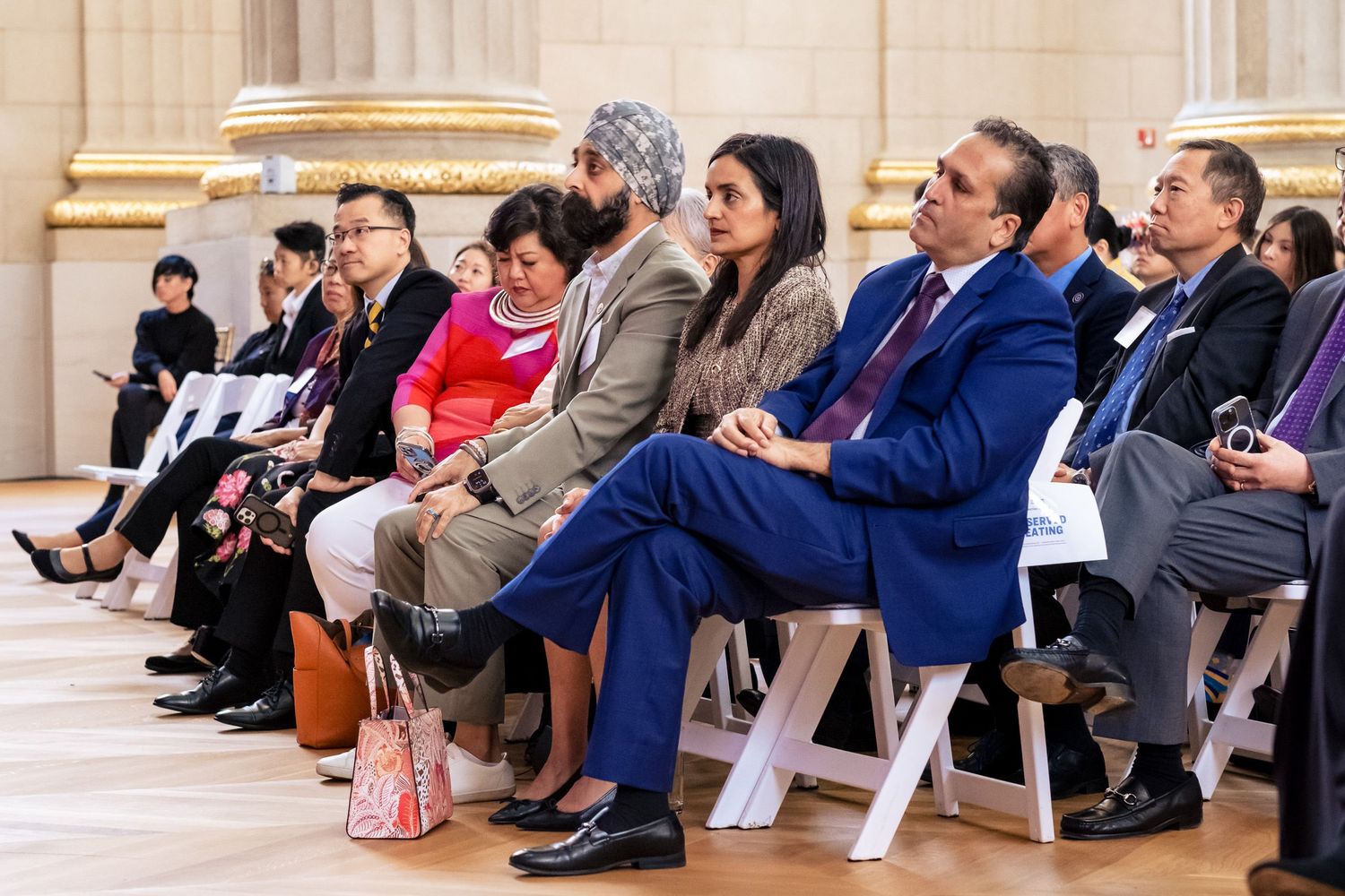 Diverse group of attendees seated in rows at a formal event in an elegant hall.