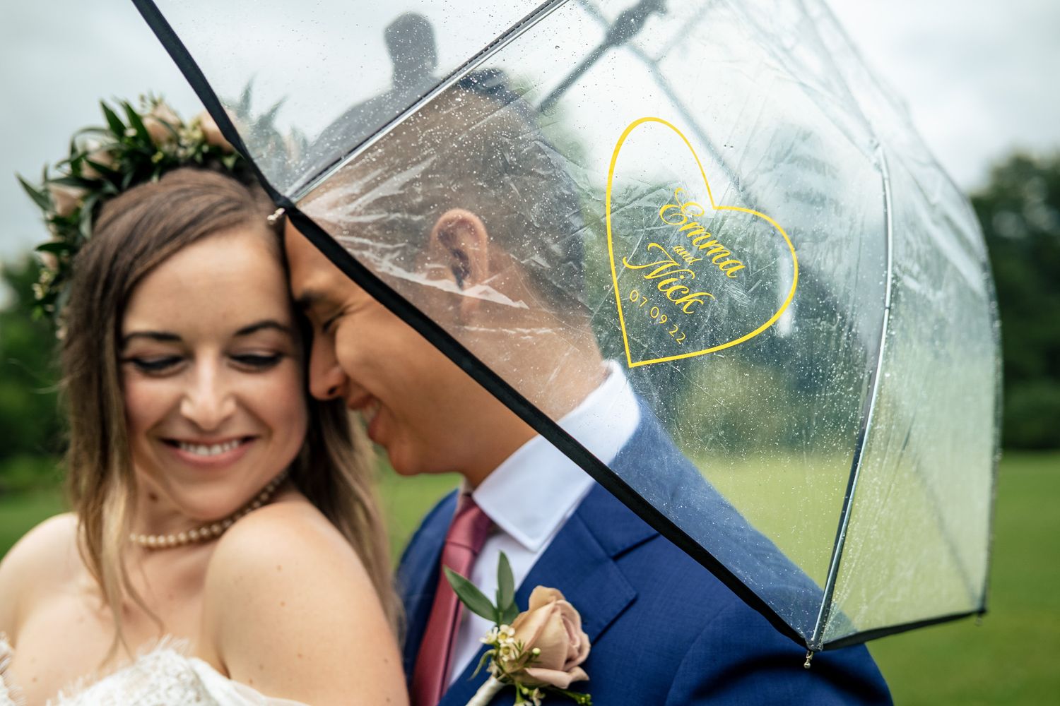 Romantic couple shares a kiss under a clear personalized umbrella on a rainy wedding day.