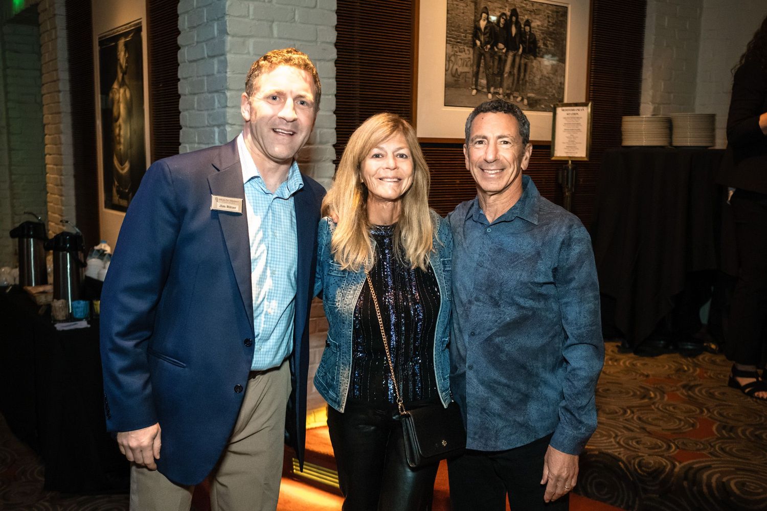 Three smiling professionals pose together at an elegant indoor networking event with artwork and ambient lighting in the background.