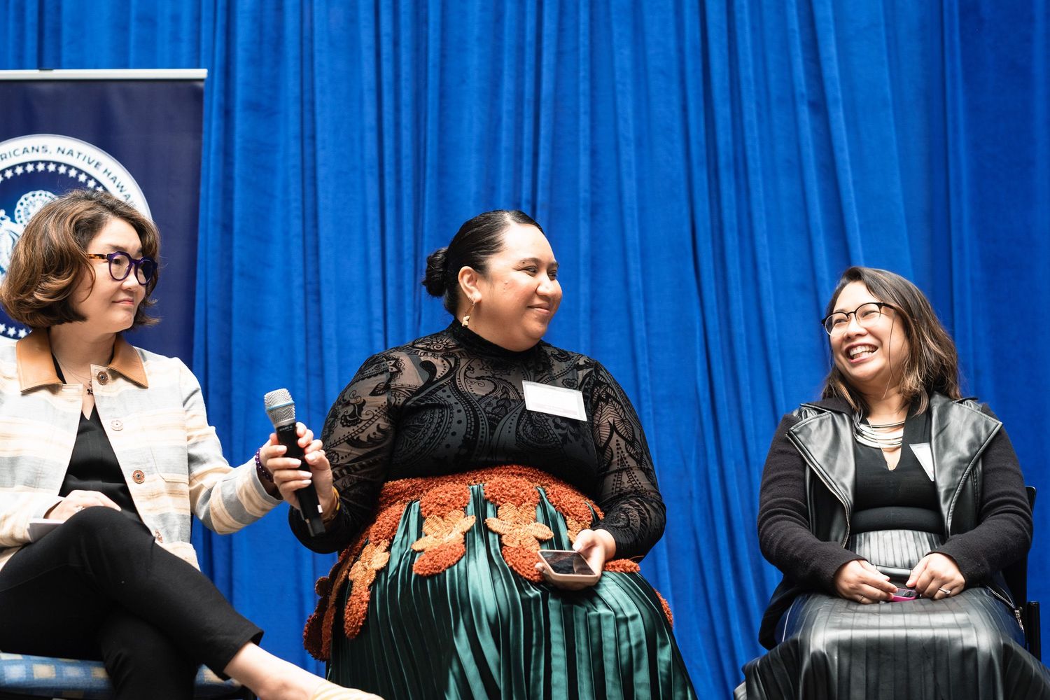 Three women laugh together on stage during a panel discussion at a cultural conference.