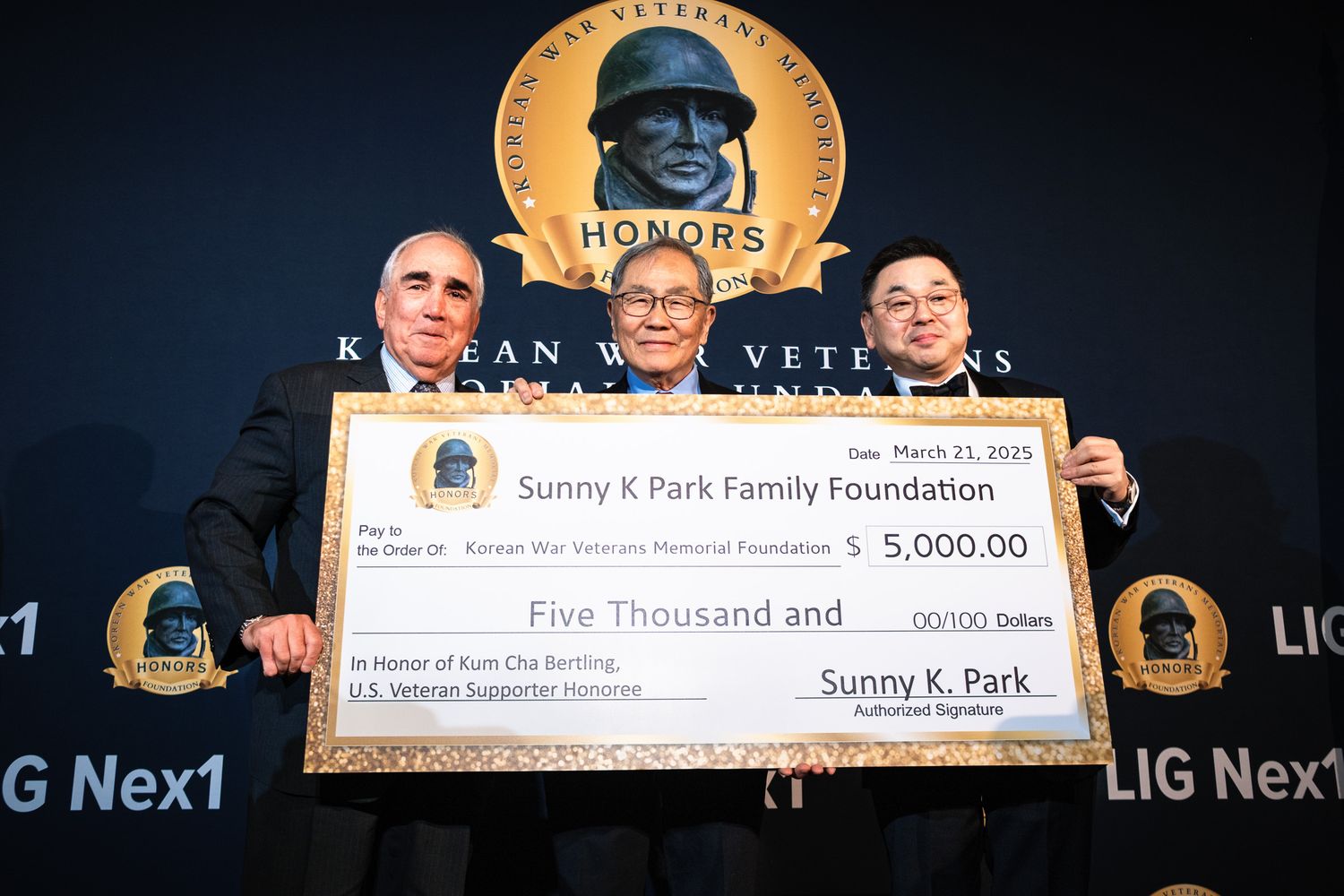 Three men hold a $5,000 ceremonial check from Sunny K Park Family Foundation at Korean War Veterans Memorial event.