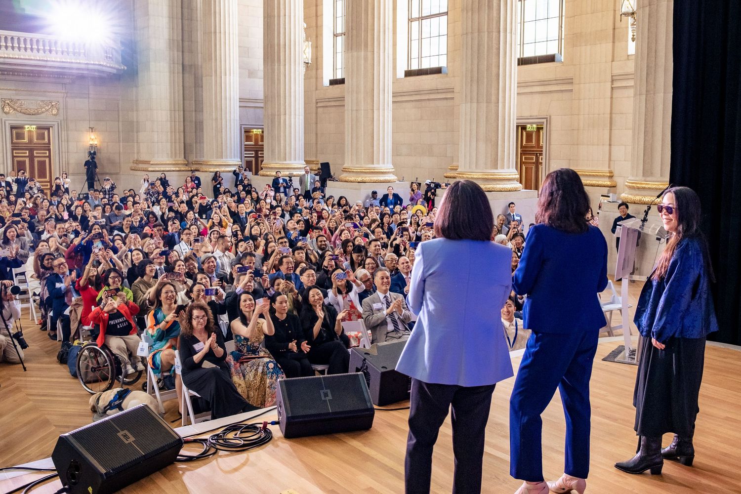 Speakers address a large audience in an elegant neoclassical hall during a professional conference event.