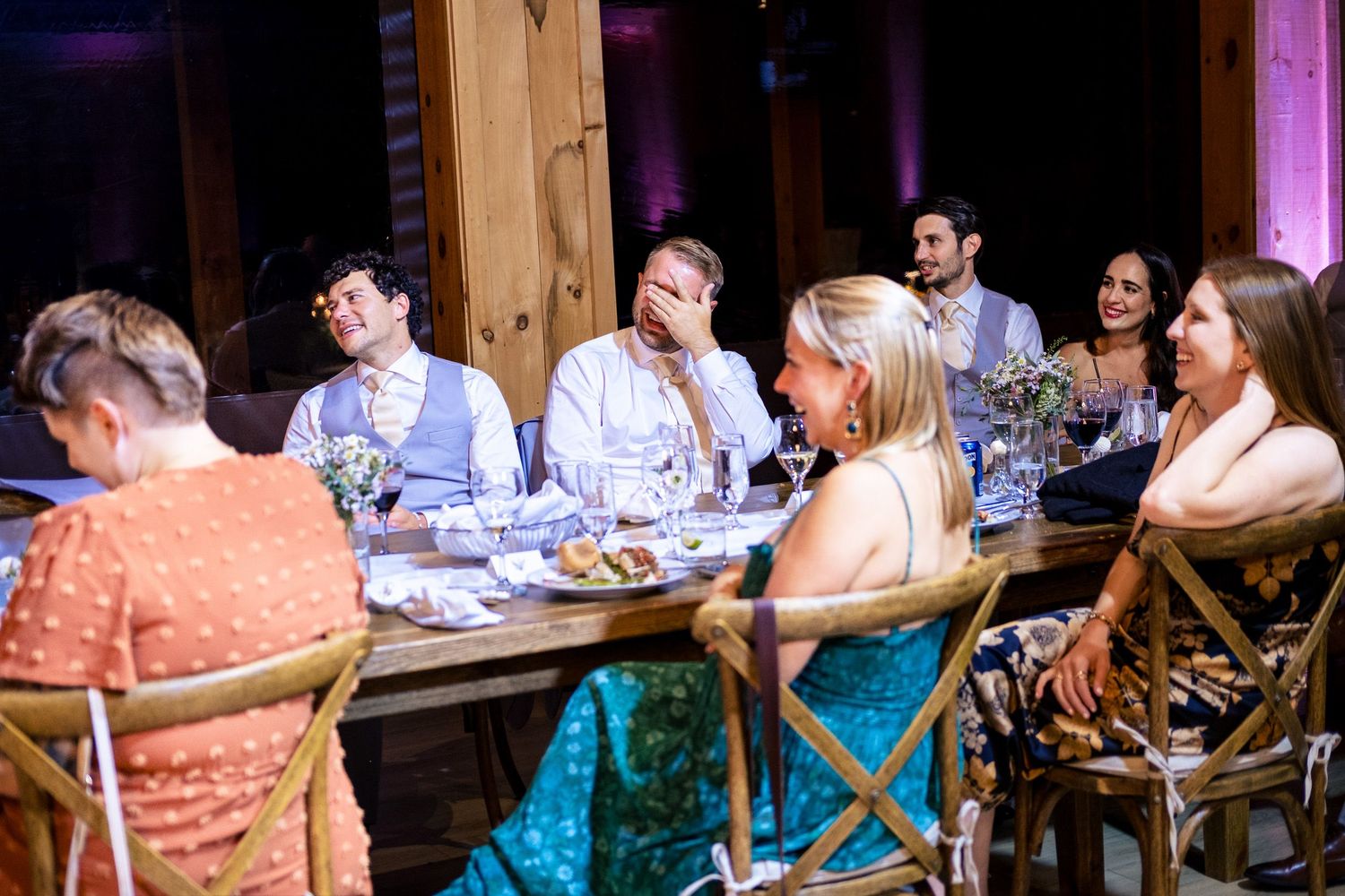 Wedding guests seated at rustic wooden table enjoying reception dinner together.
