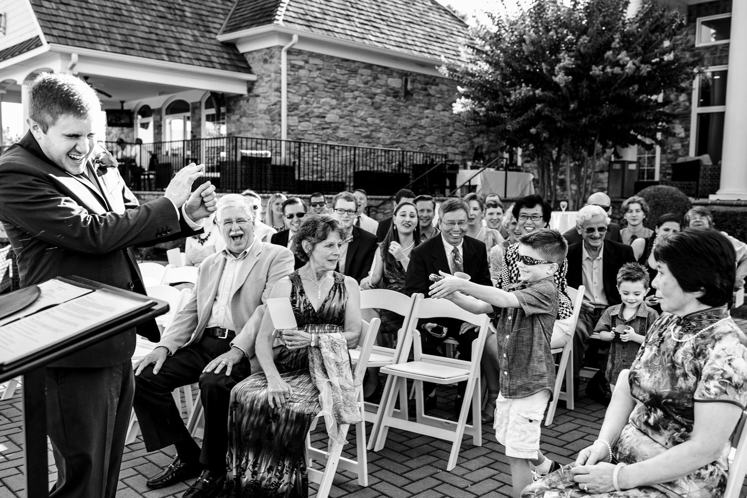 Black and white photo of wedding guests reacting with joy during an outdoor ceremony at a stone venue.