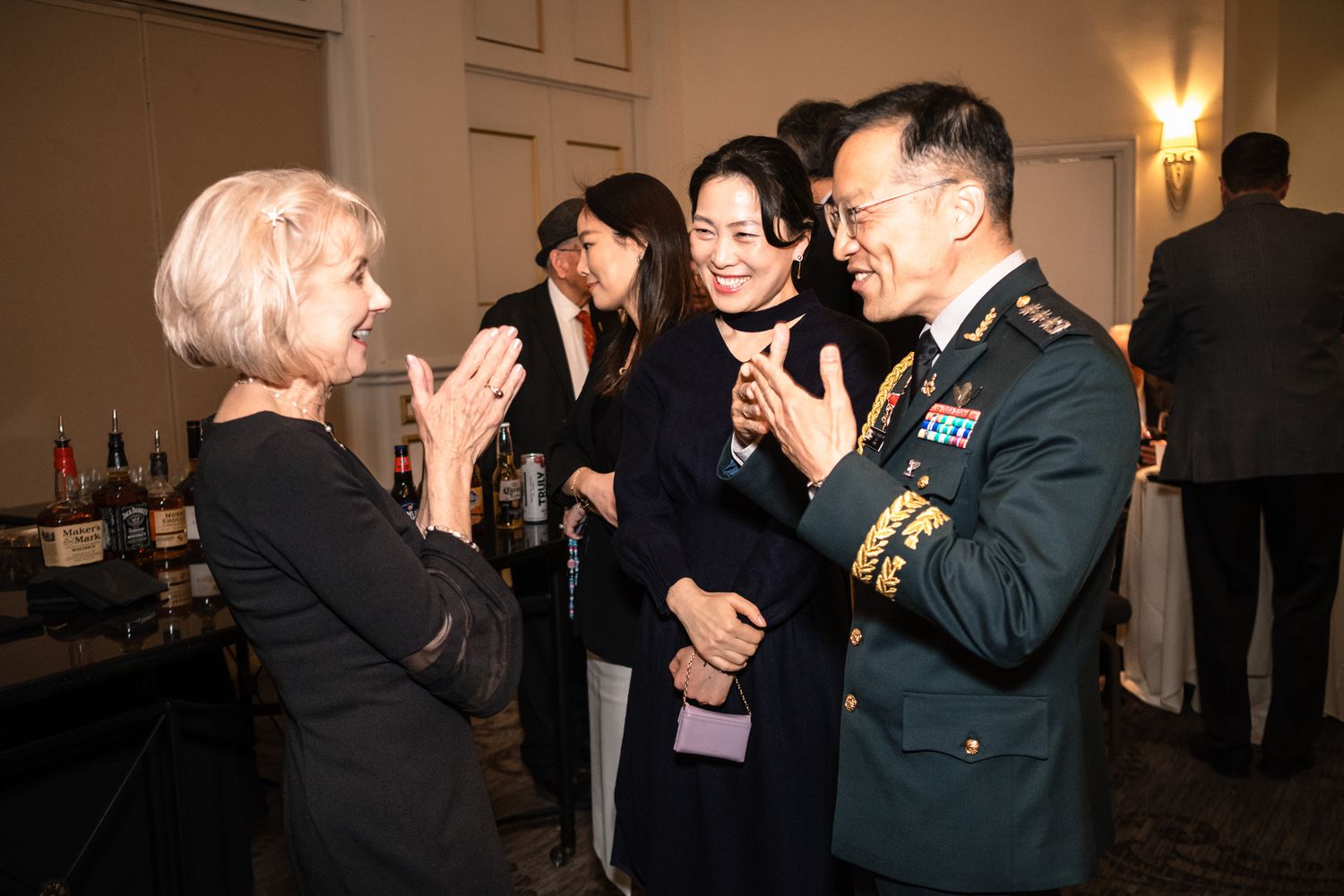 Military officer in uniform converses with elegantly dressed guests at a formal diplomatic reception event.