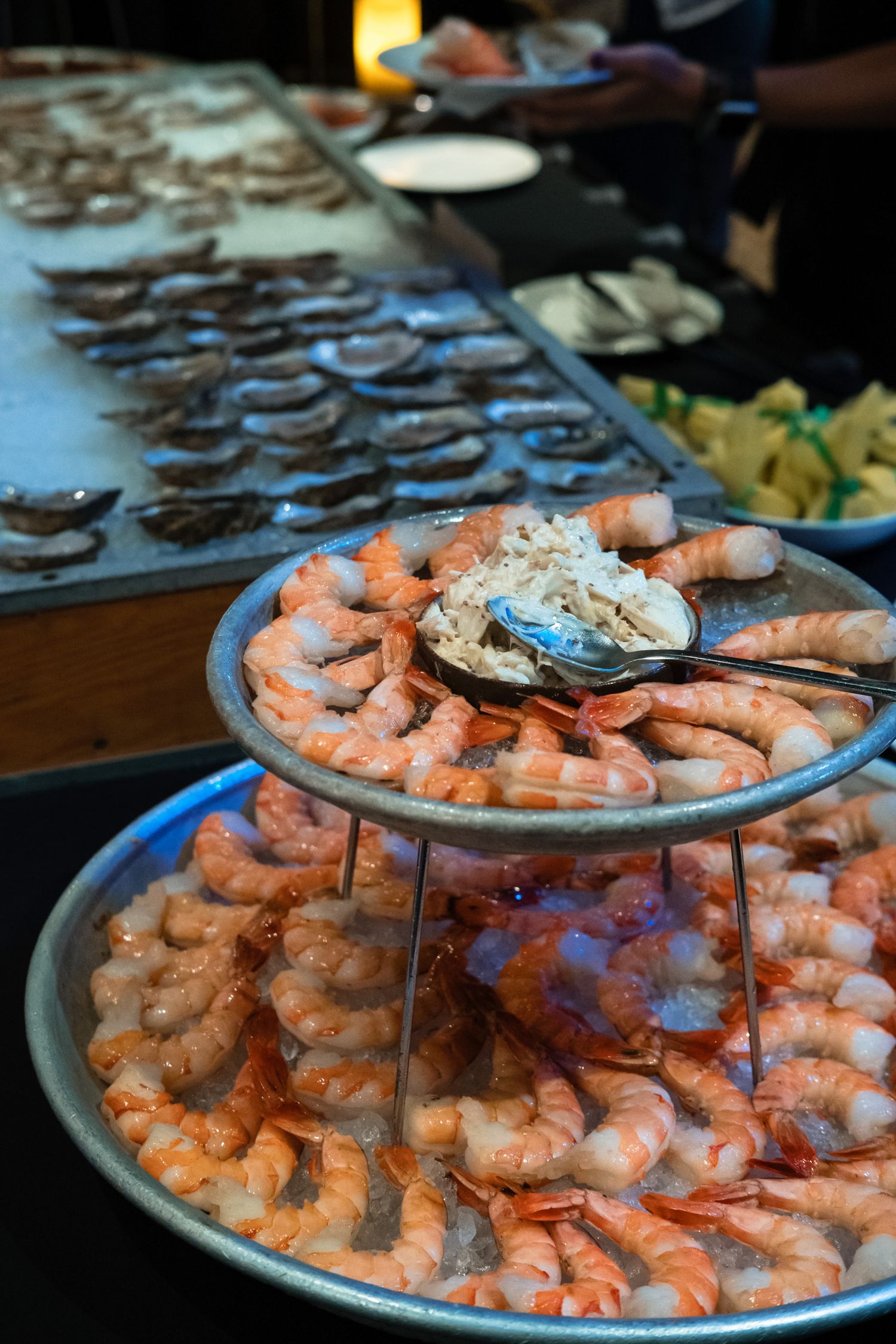 Two-tiered seafood display with shrimp on ice and oysters at a buffet restaurant.