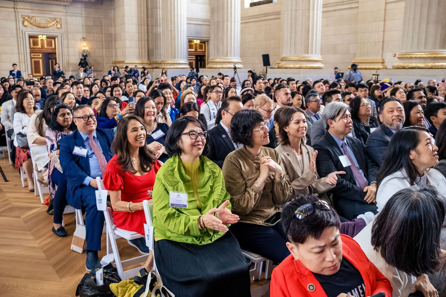 Large diverse crowd seated in an elegant hall attending a formal event or ceremony.