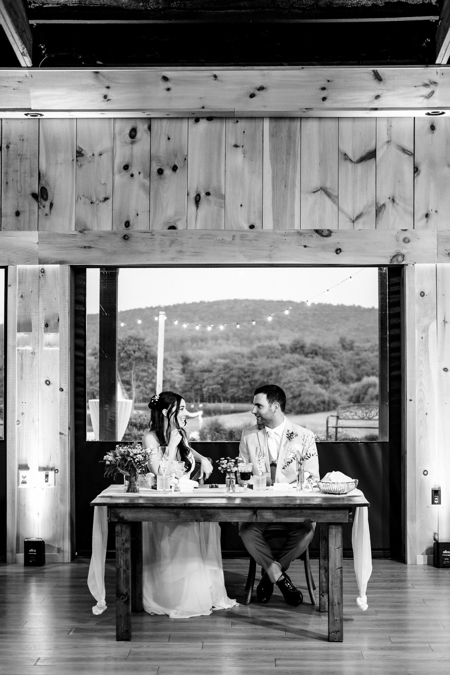 Bride and groom share an intimate moment at their sweetheart table in rustic barn venue.