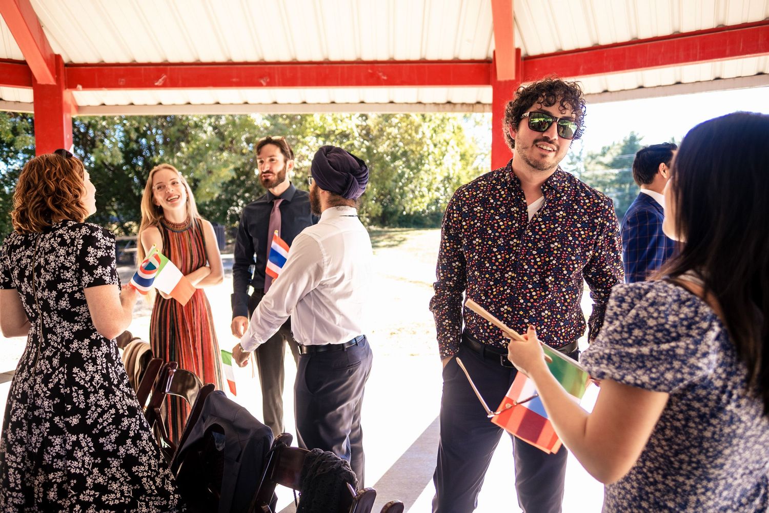 Guests mingle and socialize under a covered pavilion at a sunny outdoor wedding celebration.
