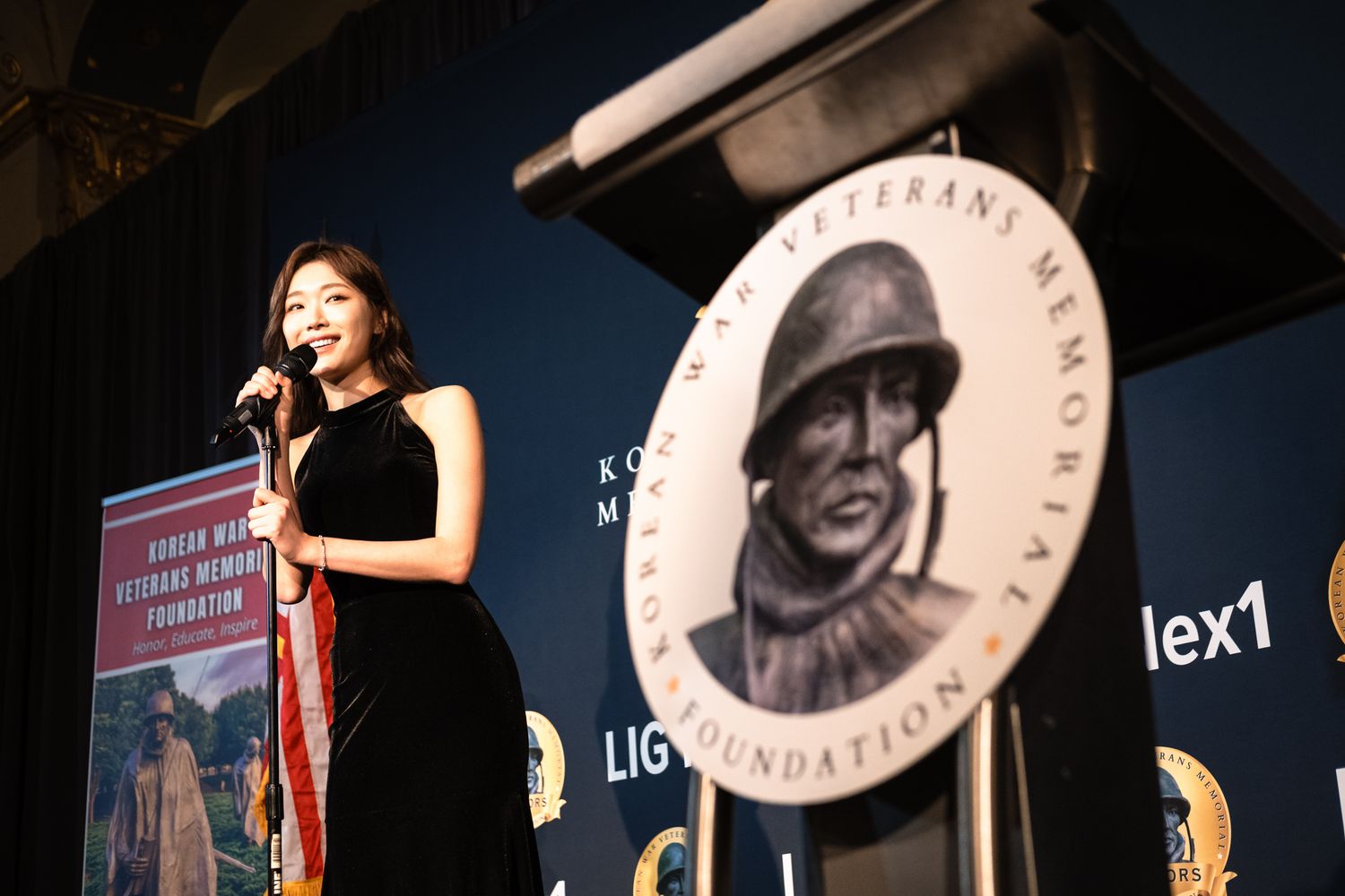 Woman in black dress speaks at podium during Korean War Veterans Memorial Foundation awards event.