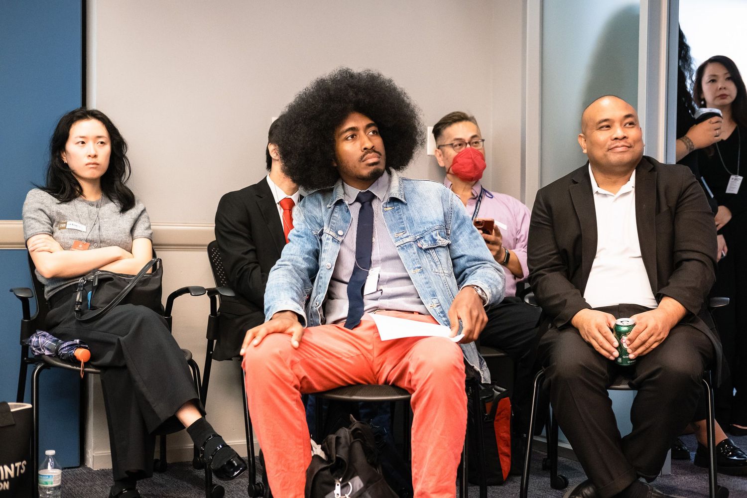 Diverse group of people seated at a professional conference or panel event in a modern office setting.