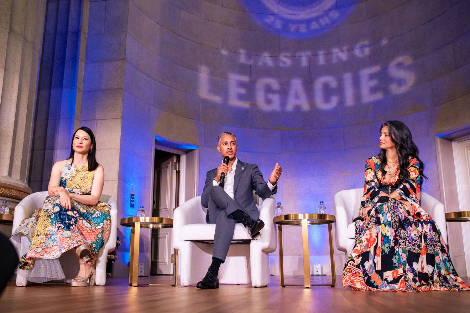 Three panelists on stage at a Lasting Legacies event, seated in white chairs under blue lighting.