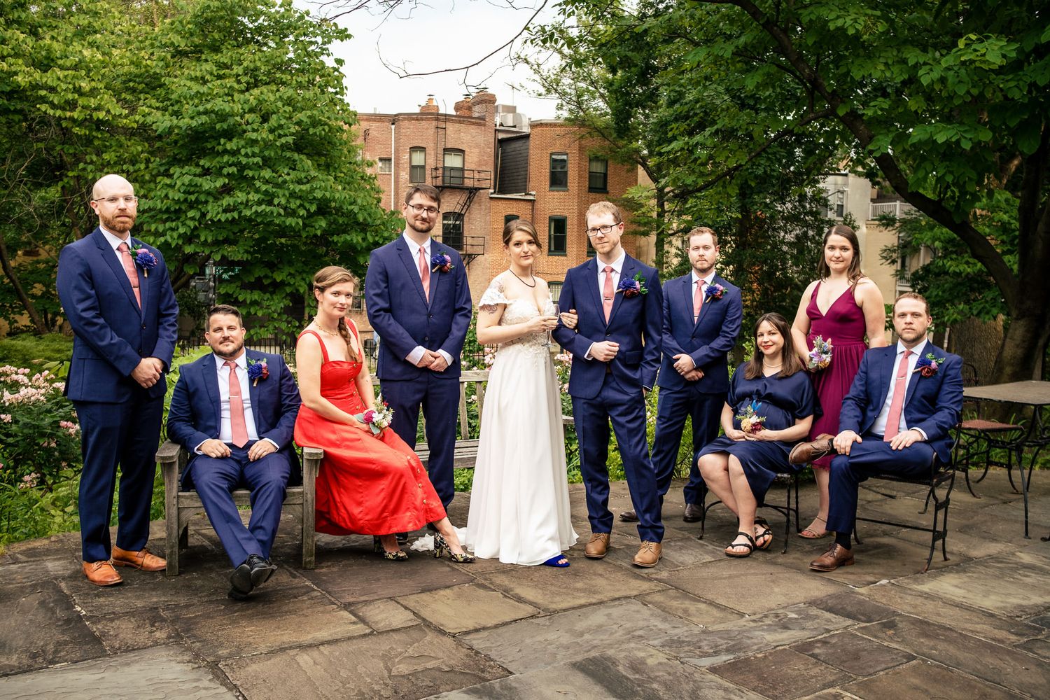 Wedding party posing together in a garden courtyard with string lights and brick buildings.