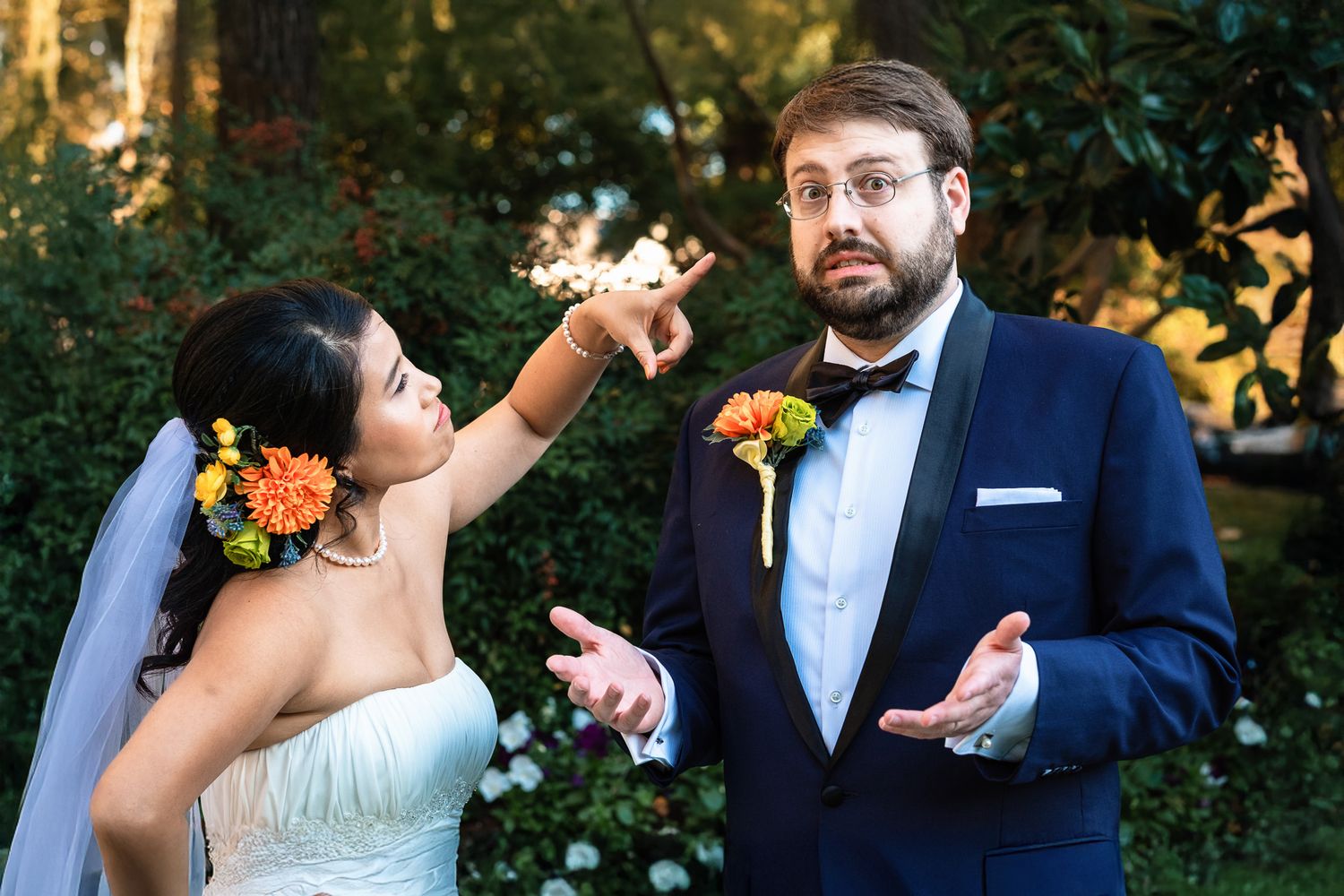 Bride playfully holds a sparkler near surprised groom with colorful floral accessories in garden setting.