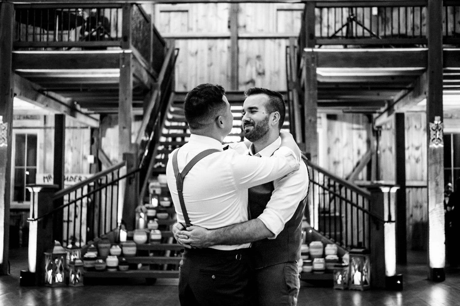 Two grooms share a romantic first dance in black and white at their barn wedding.