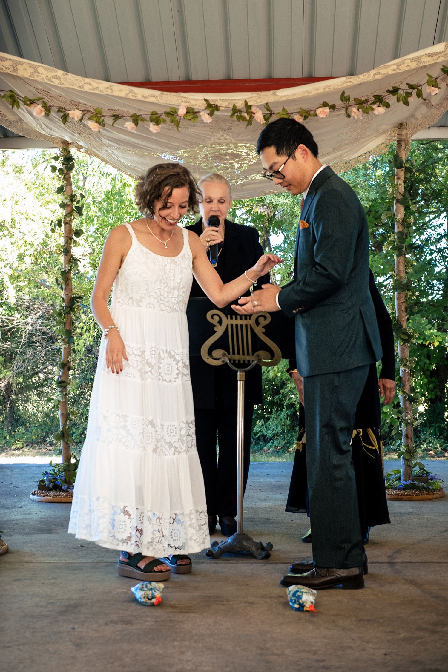 Bride and groom prepare to stomp on glasses in traditional Jewish wedding ceremony under floral arch.