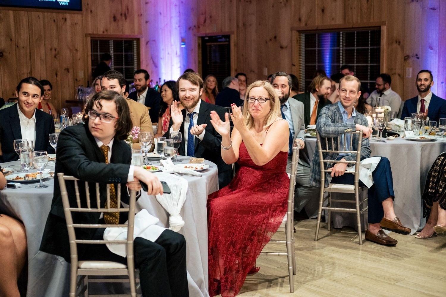 Wedding reception guests applauding and celebrating in rustic barn venue.
