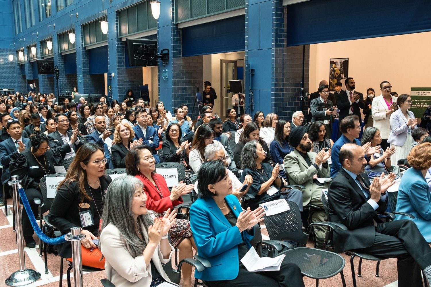 Large diverse audience applauding at an indoor conference event in a modern venue with blue walls.