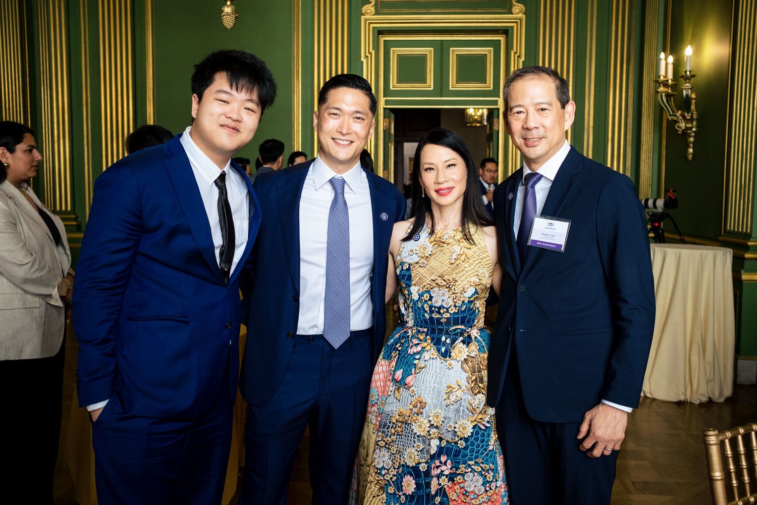 Four elegantly dressed guests smiling together at a formal event in a green-walled ballroom.